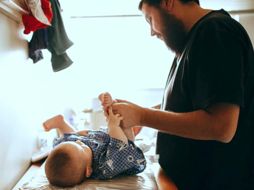 Dad changing his childs diaper on a changing table