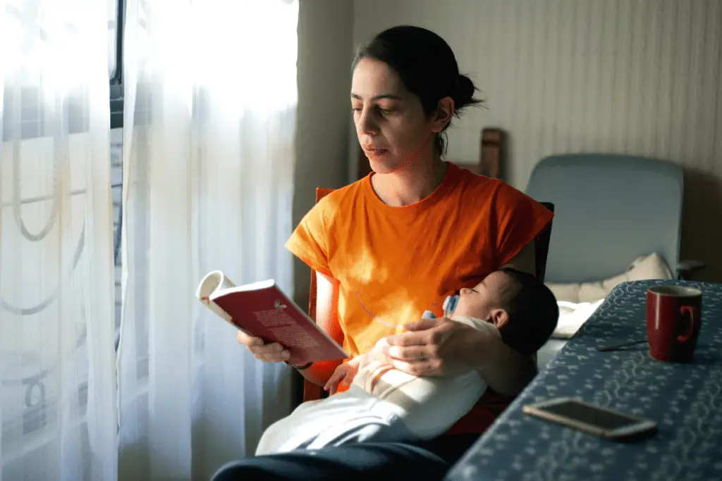 new mom reading a book with sleeping baby on her arms