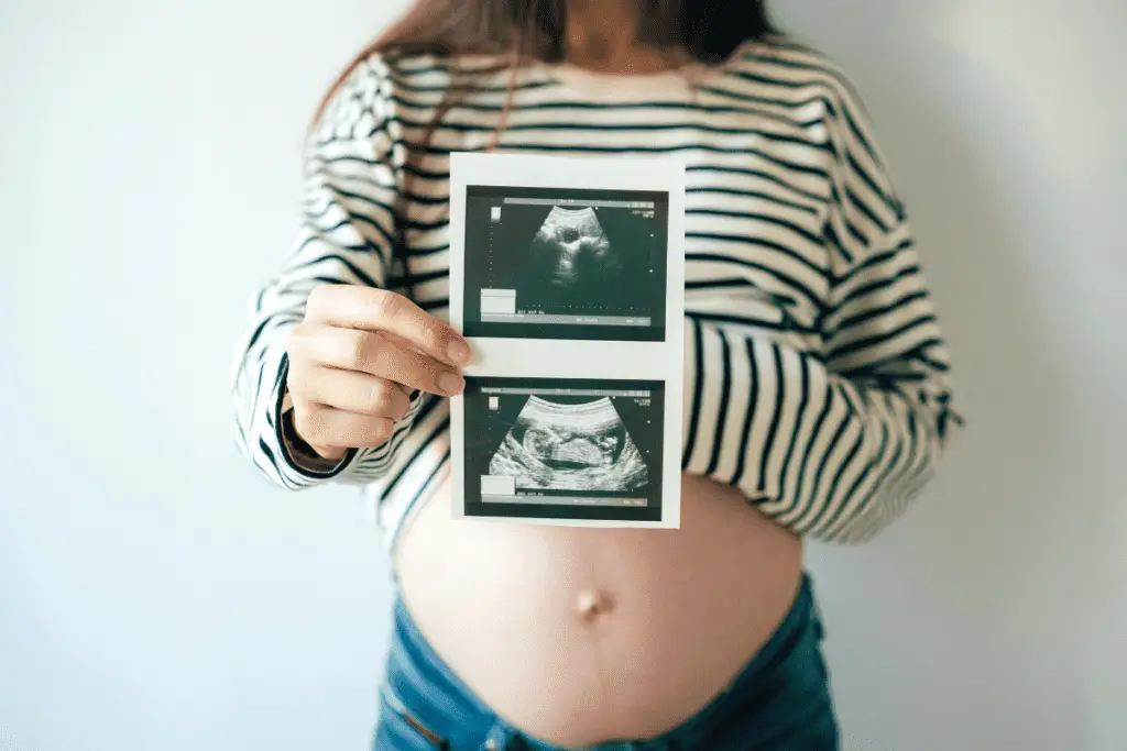 woman showing her pregnant belly and holding up ultrasound pictures of her baby